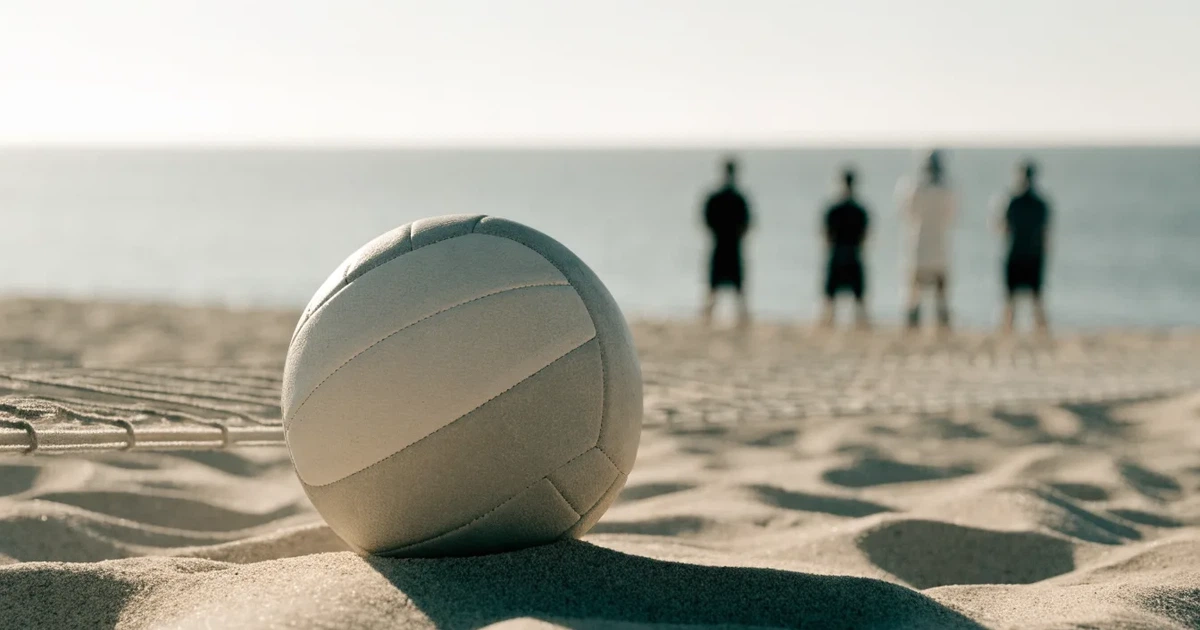Ein Volleyball liegt auf feinem hellem Sand, ein gespanntes Netz verschwimmt dahinter, das Licht kommt von einem weiten Meer.