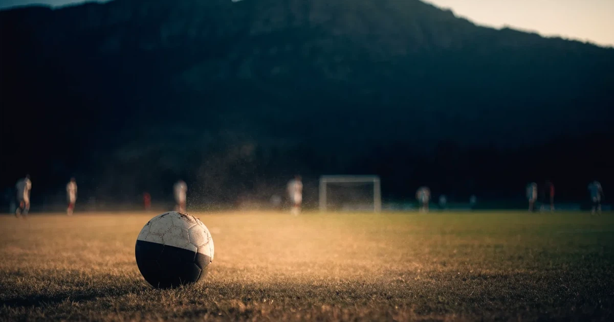 Ein Fussball auf einem staubigen Rasenstück in der Abendsonne, im Hintergrund eine hohe Bergkette
