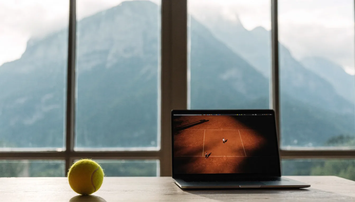 Ein einzelner gelber Tennisball liegt auf einem Holztisch vor einem Fenster mit Alpenblick