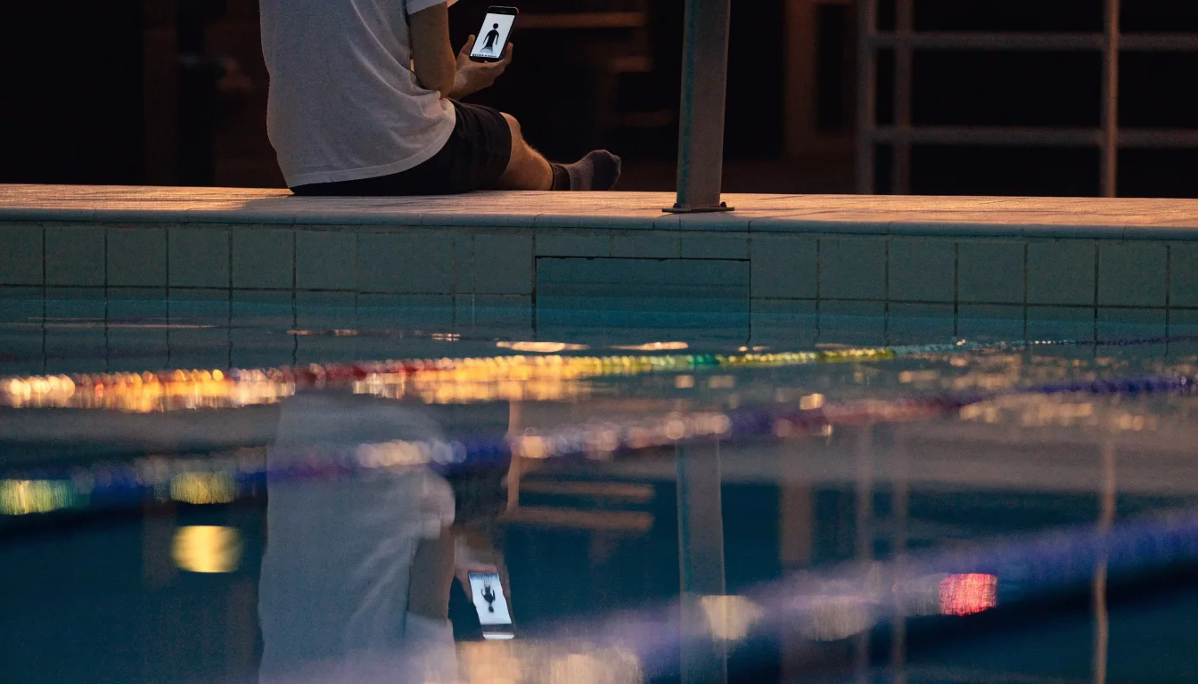 Ein Bademeisterstuhl neben einem Hallenbad zur Schliesszeit, gedimmtes Licht, glatte Wasseroberfläche.