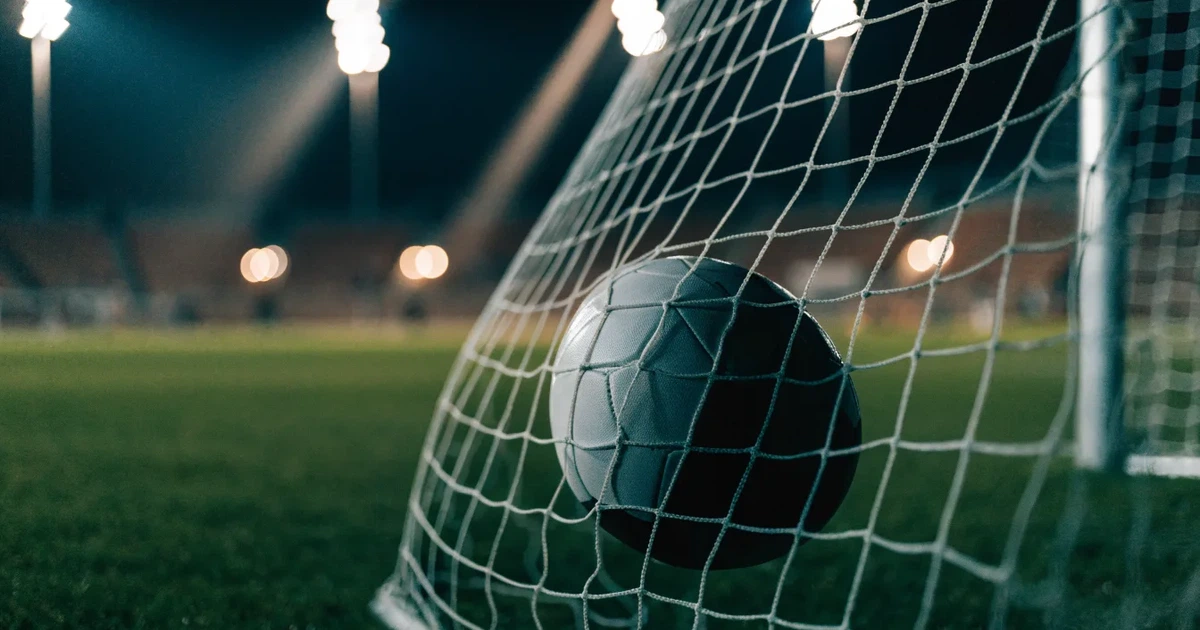 Ein Fussball liegt im Netz eines Tores, Flutlicht und kalte Abendluft liegen über dem leeren Platz