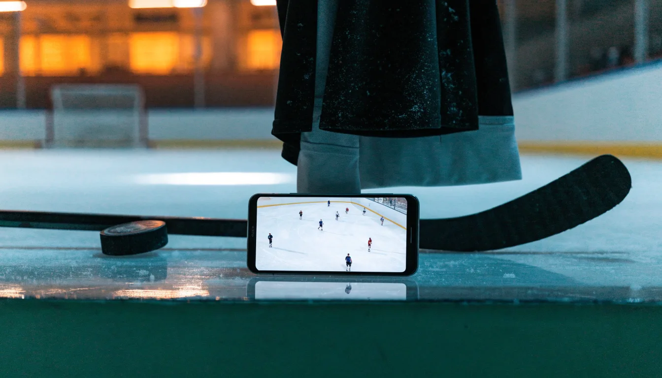 Ein Eishockeypuck und ein Schläger liegen auf einer glänzenden Eisfläche, im Hintergrund verschwimmen leere Banden.