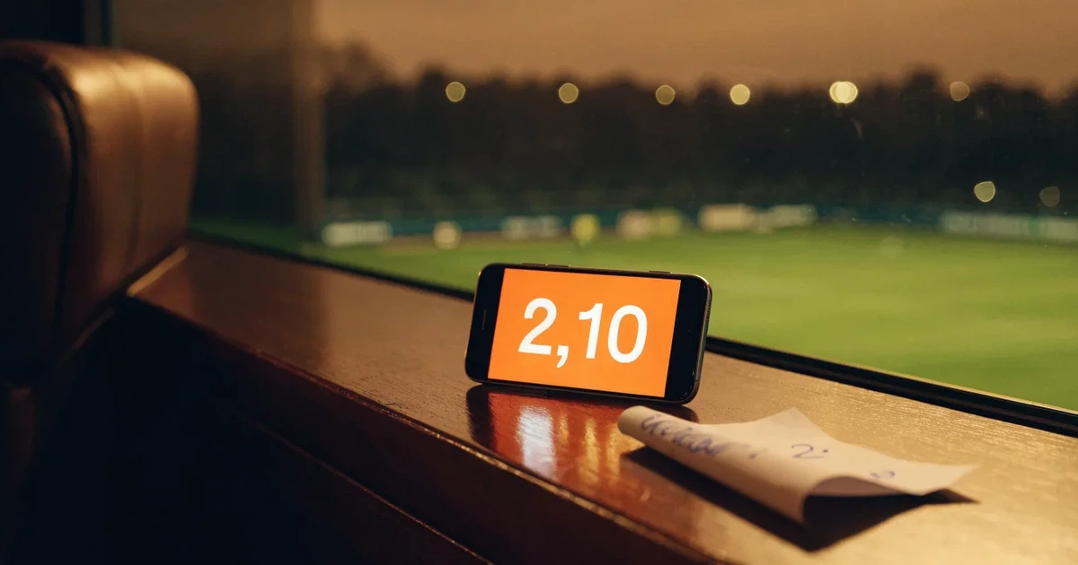 Ein leerer Ledersessel steht in einer Stadionloge mit Blick auf das Spielfeld im Abendlicht.